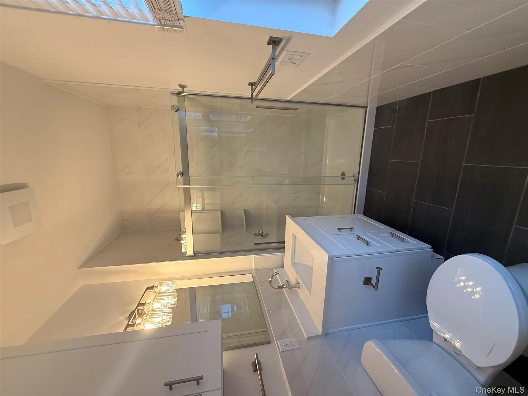 Full bath with tile walls, a shower stall, vanity, dark tile patterned floors, and a wainscoted wall Full bath with tile walls, a shower stall, vanity, dark tile patterned floors, and a wainscoted wall