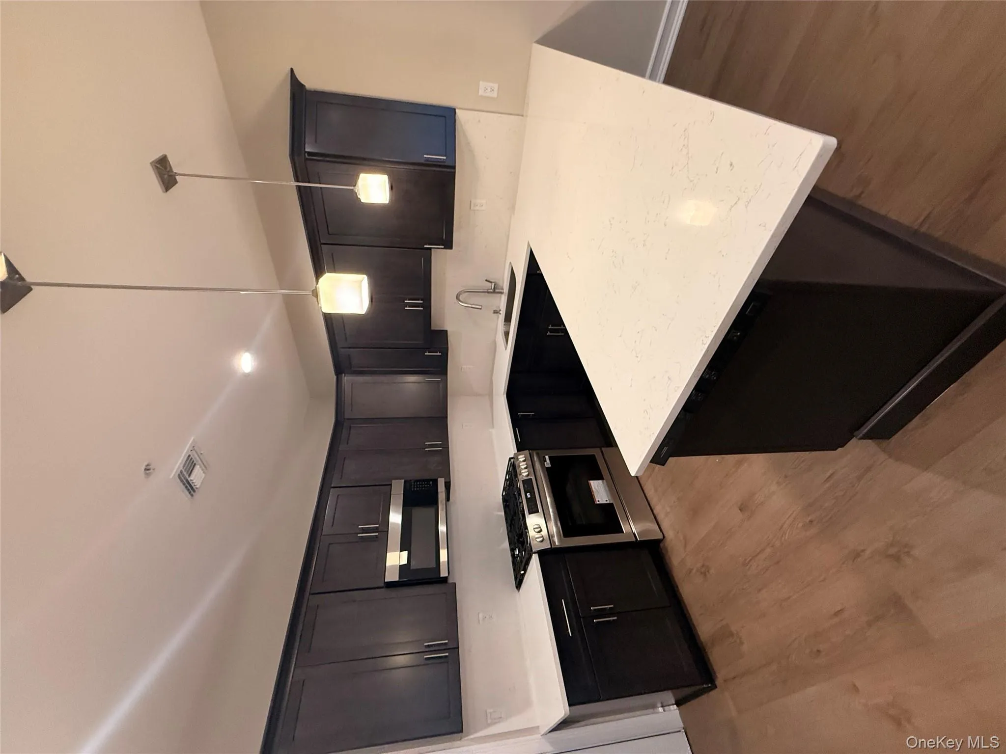 Kitchen featuring stainless steel stove, a peninsula, hanging light fixtures, light stone counters, and light wood-type flooring Kitchen featuring stainless steel stove, a peninsula, hanging light fixtures, light stone counters, and light wood-type flooring
