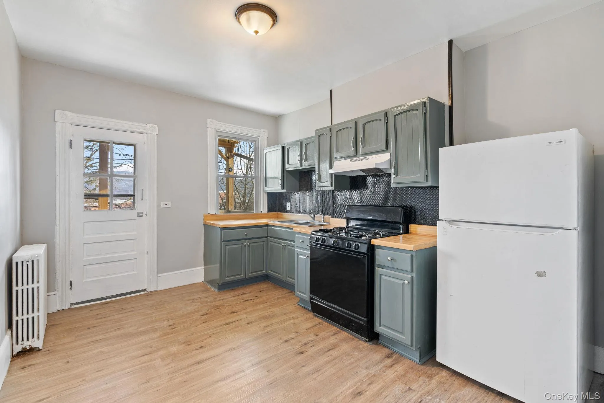 Kitchen featuring freestanding refrigerator, black gas range, radiator, backsplash, and under cabinet range hood Kitchen featuring freestanding refrigerator, black gas range, radiator, backsplash, and under cabinet range hood