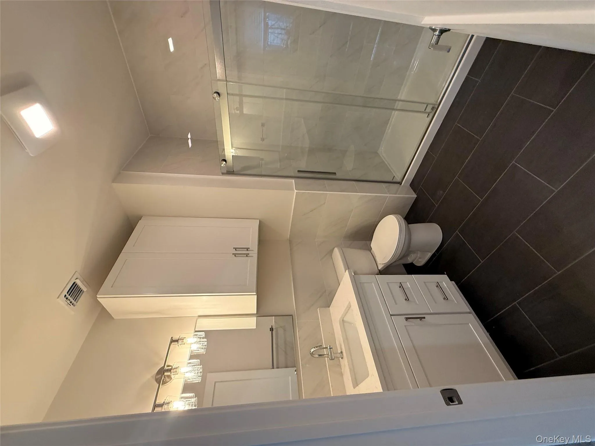 Bathroom with a shower stall, vanity, tile walls, and dark tile patterned floors Bathroom with a shower stall, vanity, tile walls, and dark tile patterned floors