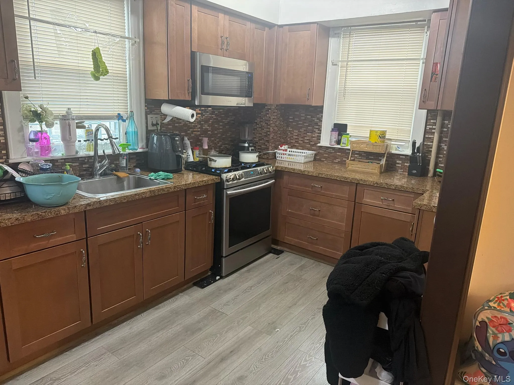 Kitchen with stainless steel appliances, light wood-type flooring, decorative backsplash, and dark stone countertops Kitchen with stainless steel appliances, light wood-type flooring, decorative backsplash, and dark stone countertops