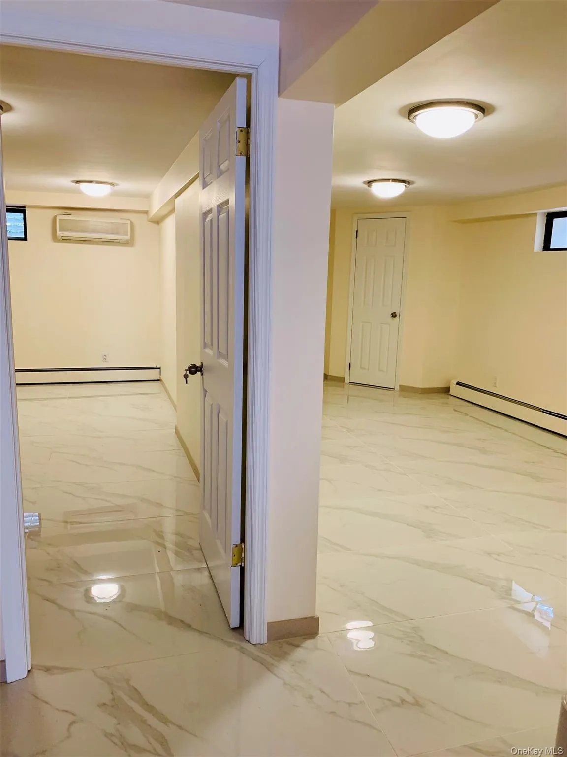 Hallway featuring light marble finish flooring, a baseboard radiator, and an AC wall unit Hallway featuring light marble finish flooring, a baseboard radiator, and an AC wall unit