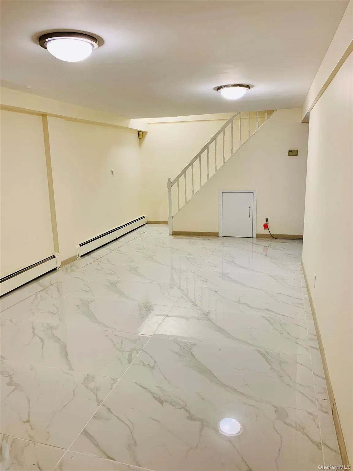 Basement featuring baseboard heating, stairway, and light marble finish flooring Basement featuring baseboard heating, stairway, and light marble finish flooring