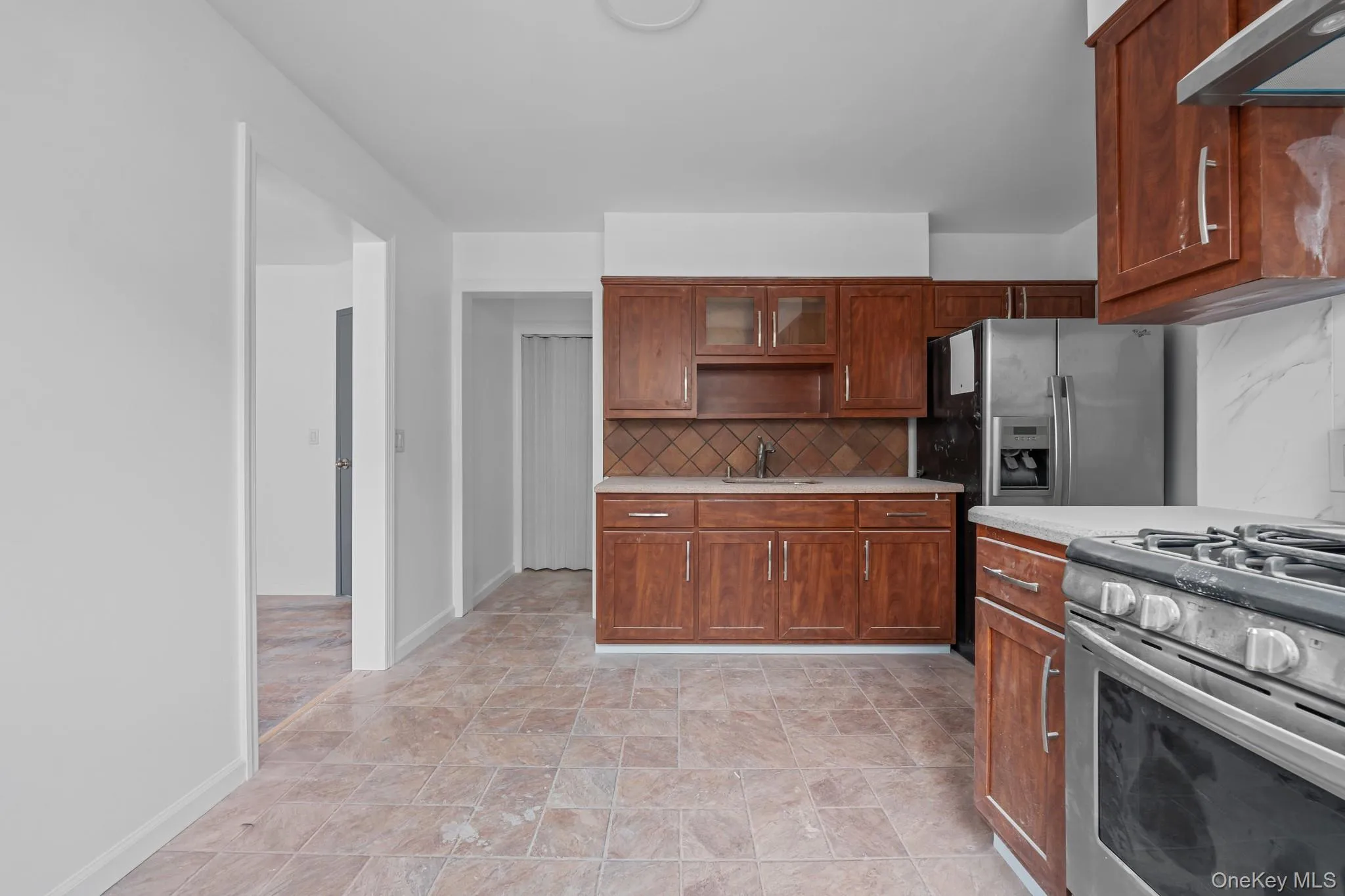 Kitchen with stainless steel appliances, glass insert cabinets, decorative backsplash, exhaust hood, and brown cabinetry Kitchen with stainless steel appliances, glass insert cabinets, decorative backsplash, exhaust hood, and brown cabinetry