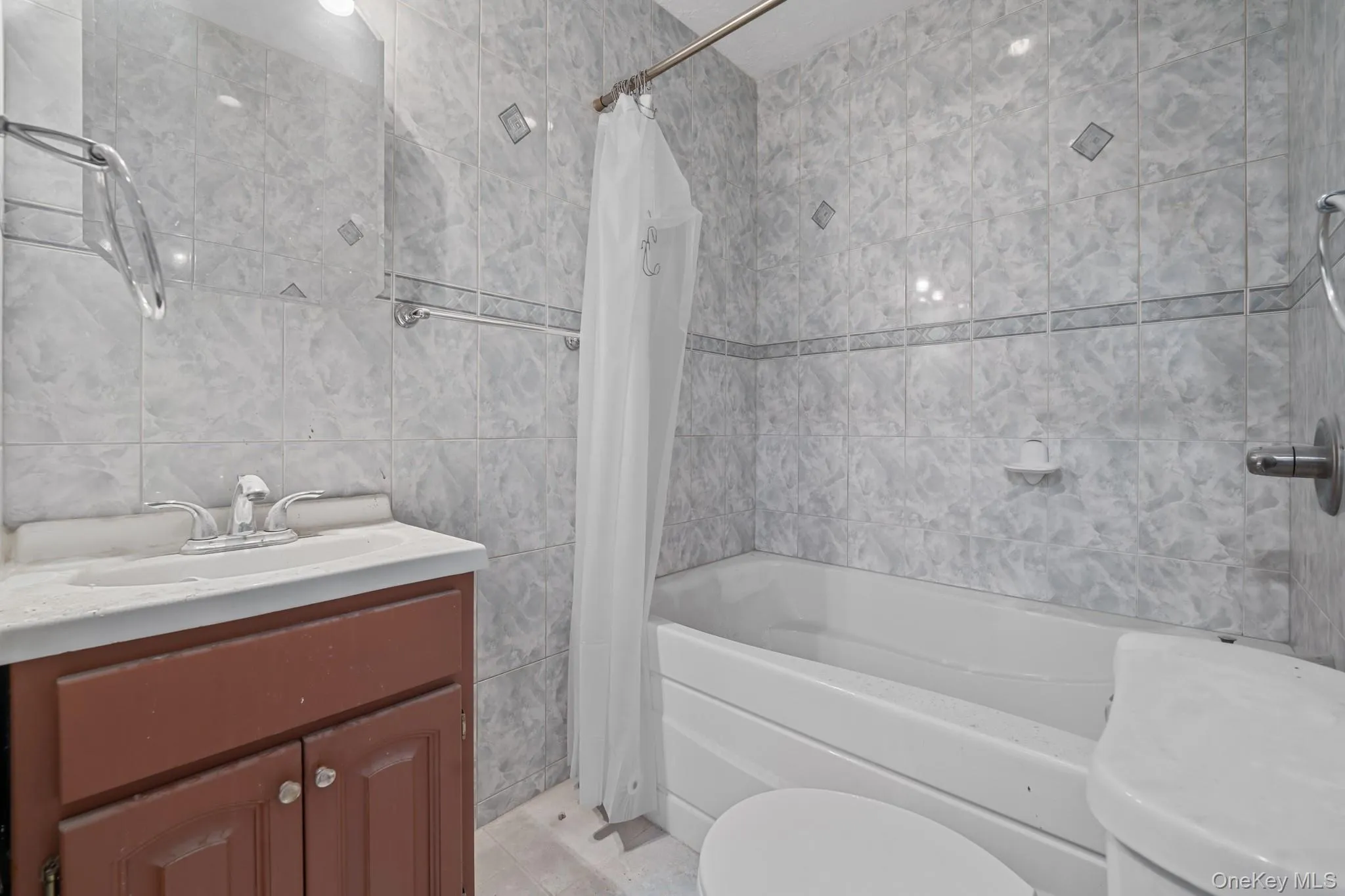 Bathroom featuring tile walls, vanity, and shower / bathtub combination with curtain Bathroom featuring tile walls, vanity, and shower / bathtub combination with curtain