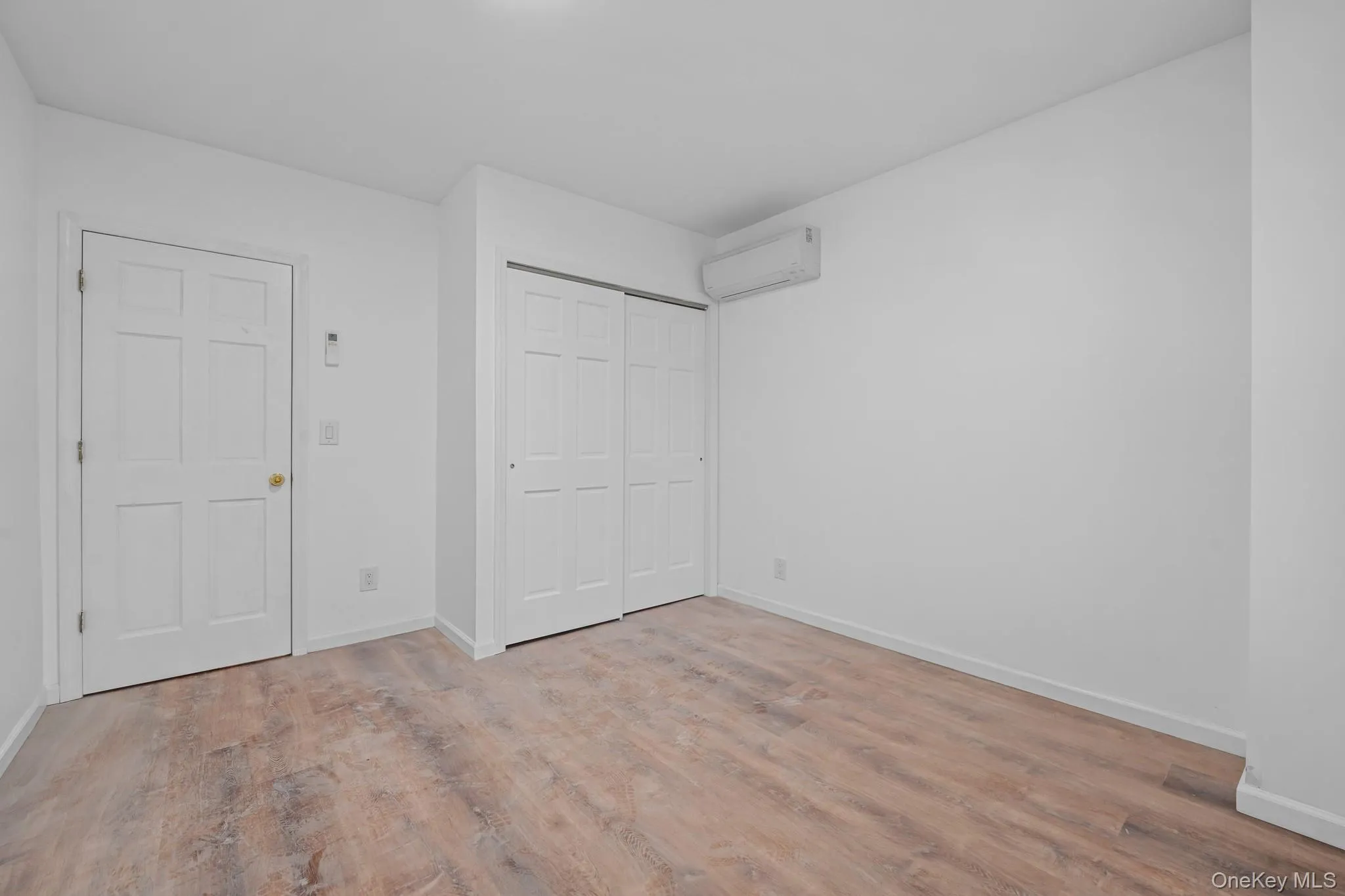 Unfurnished bedroom featuring a closet, a wall mounted air conditioner, and light wood-type flooring Unfurnished bedroom featuring a closet, a wall mounted air conditioner, and light wood-type flooring