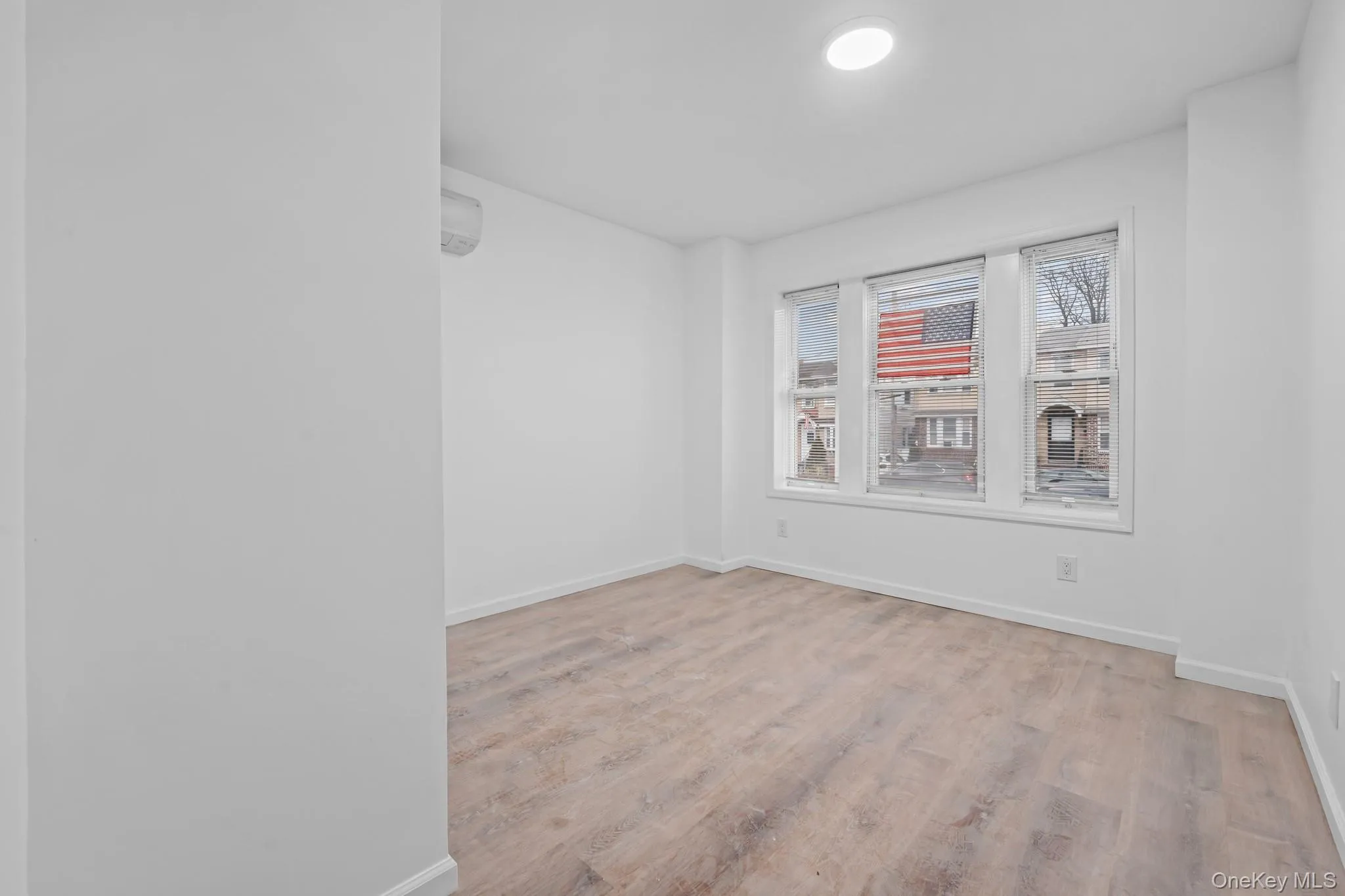 Empty room with light wood-style flooring and an AC wall unit Empty room with light wood-style flooring and an AC wall unit
