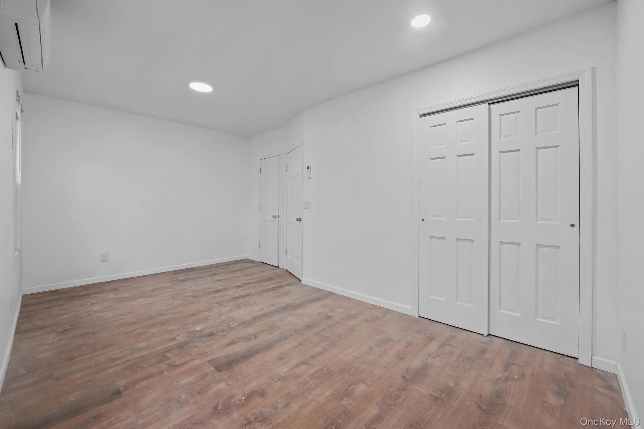 Unfurnished bedroom featuring a wall mounted air conditioner, recessed lighting, wood finished floors, and two closets Unfurnished bedroom featuring a wall mounted air conditioner, recessed lighting, wood finished floors, and two closets
