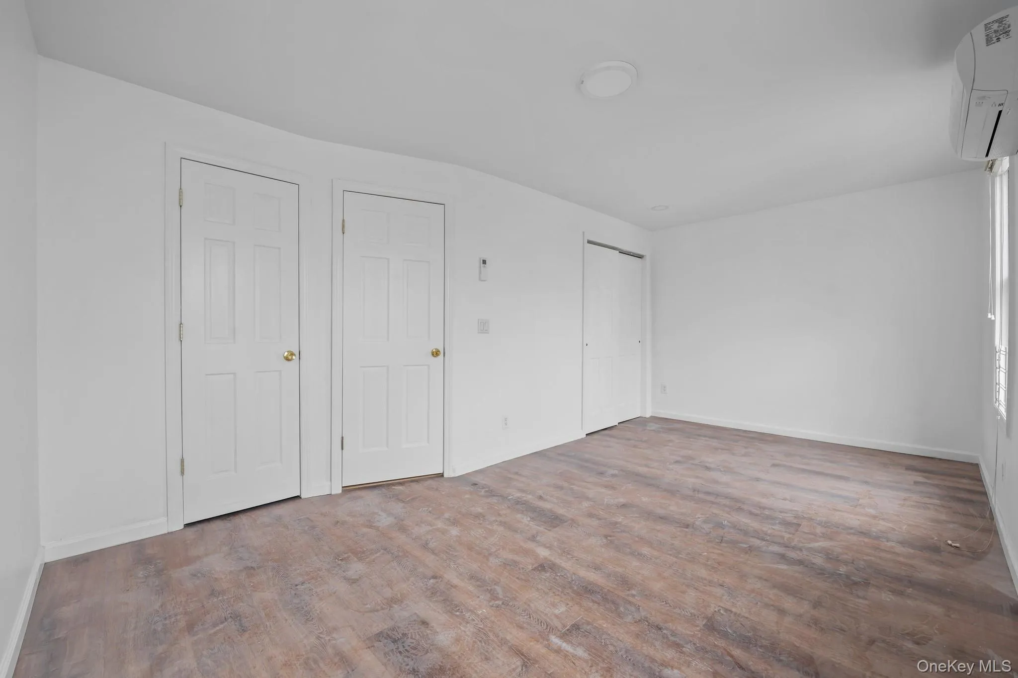 Unfurnished bedroom with a wall unit AC and wood finished floors Unfurnished bedroom with a wall unit AC and wood finished floors
