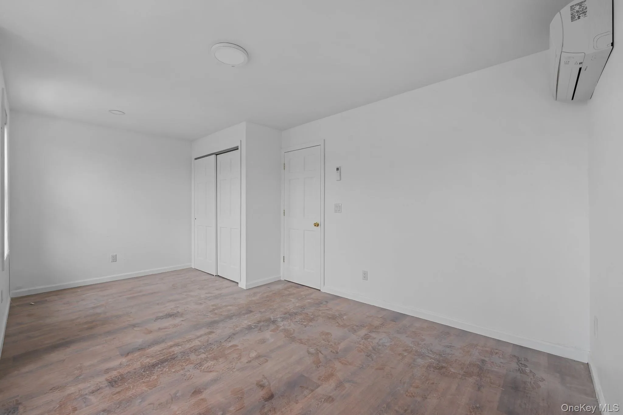 Unfurnished bedroom featuring a wall unit AC, a closet, and wood finished floors Unfurnished bedroom featuring a wall unit AC, a closet, and wood finished floors