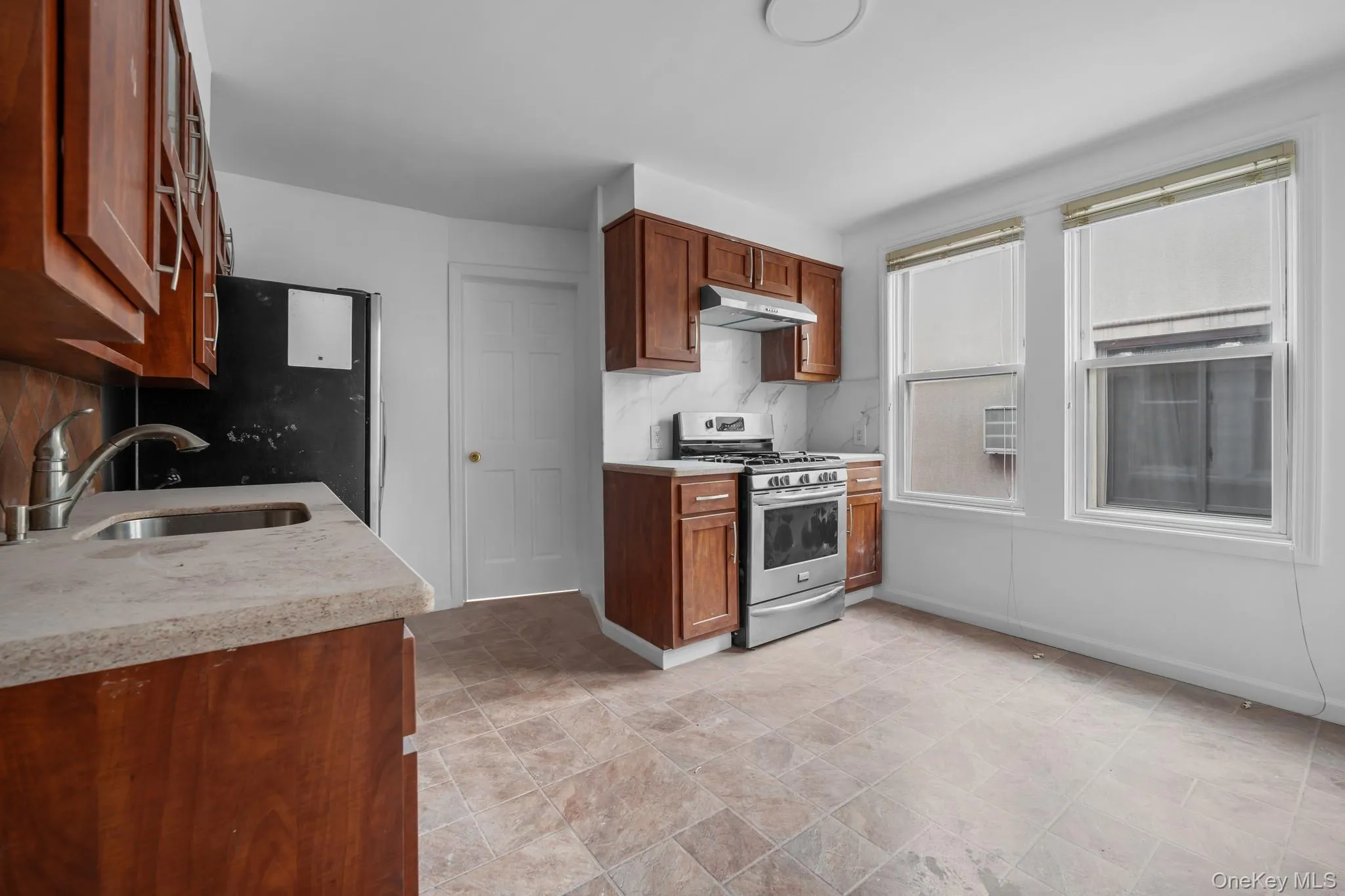 Kitchen with stainless steel gas range oven, brown cabinetry, stone finish floors, under cabinet range hood, and decorative backsplash Kitchen with stainless steel gas range oven, brown cabinetry, stone finish floors, under cabinet range hood, and decorative backsplash