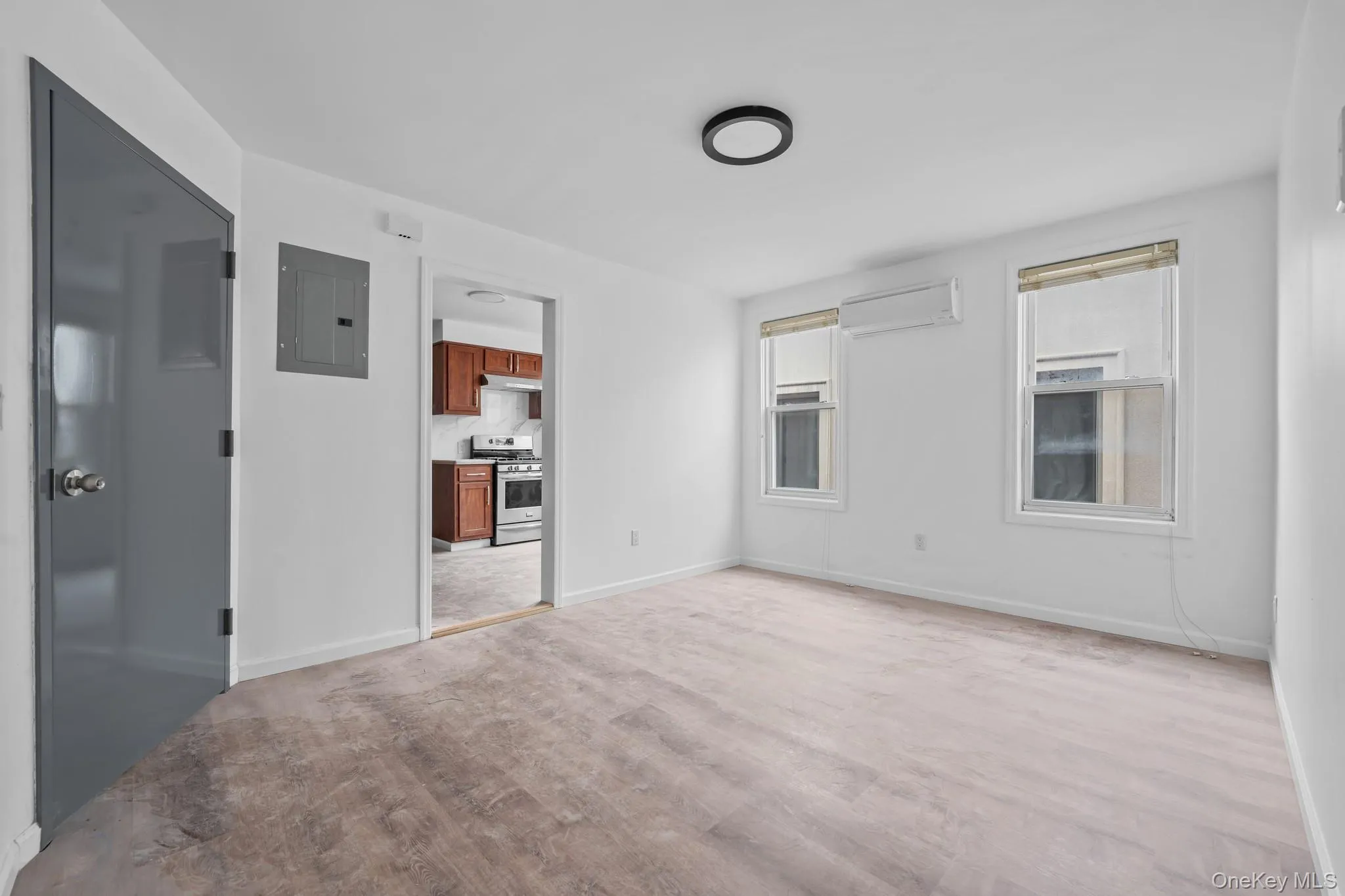 Spare room with electric panel, light wood-style floors, and an AC wall unit Spare room with electric panel, light wood-style floors, and an AC wall unit