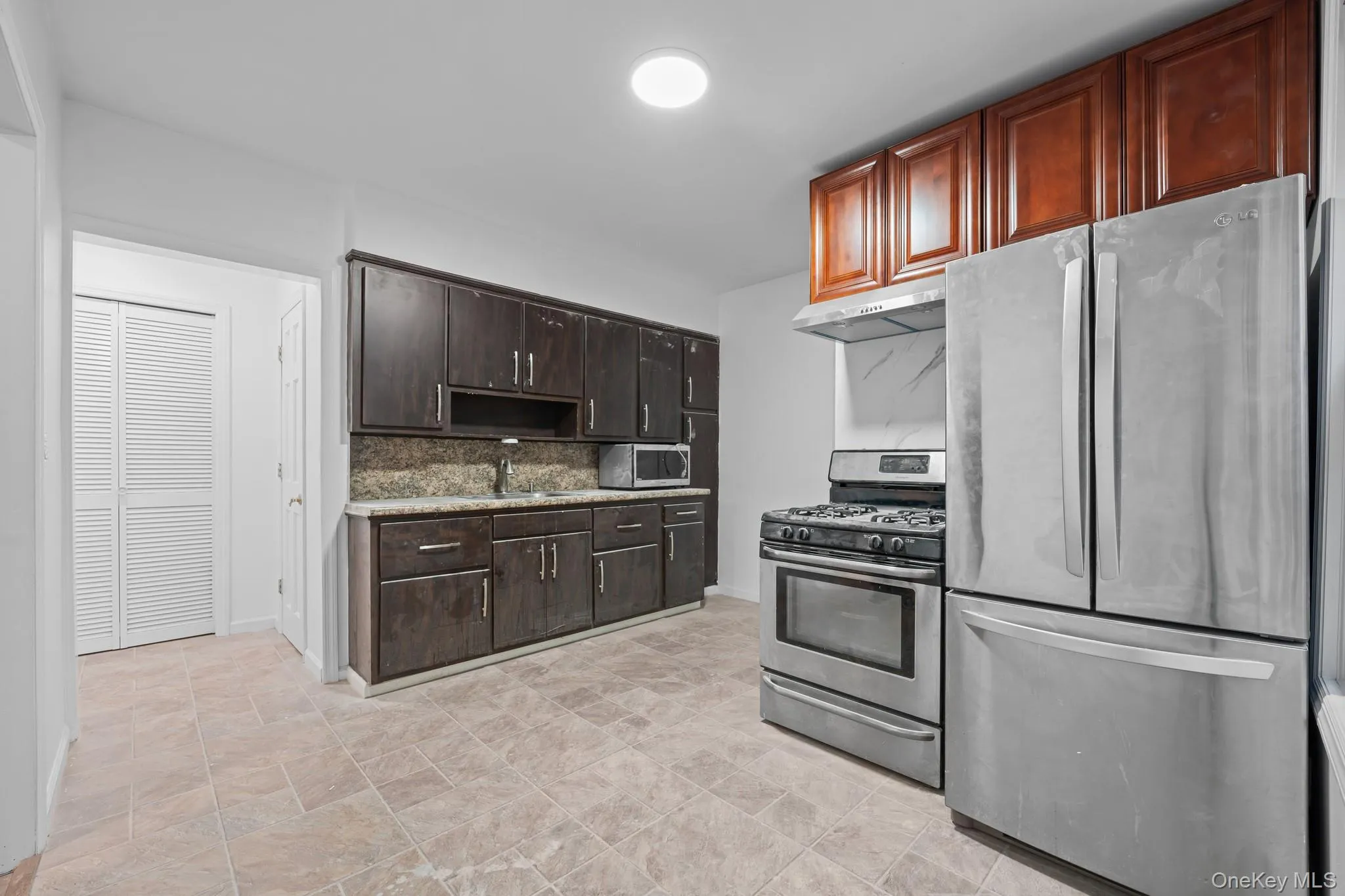 Kitchen with appliances with stainless steel finishes, backsplash, dark brown cabinets, under cabinet range hood, and stone finish flooring Kitchen with appliances with stainless steel finishes, backsplash, dark brown cabinets, under cabinet range hood, and stone finish flooring