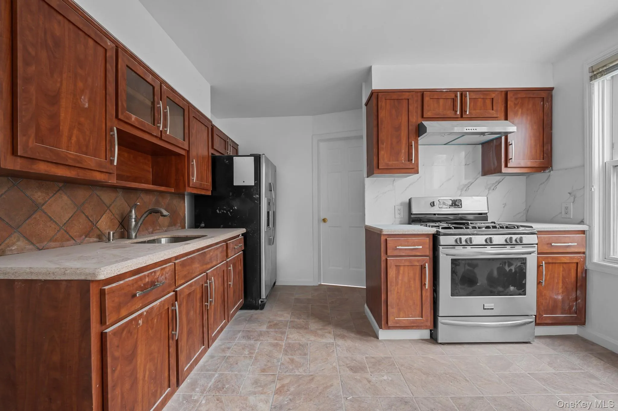 Kitchen with appliances with stainless steel finishes, backsplash, glass insert cabinets, and brown cabinets Kitchen with appliances with stainless steel finishes, backsplash, glass insert cabinets, and brown cabinets