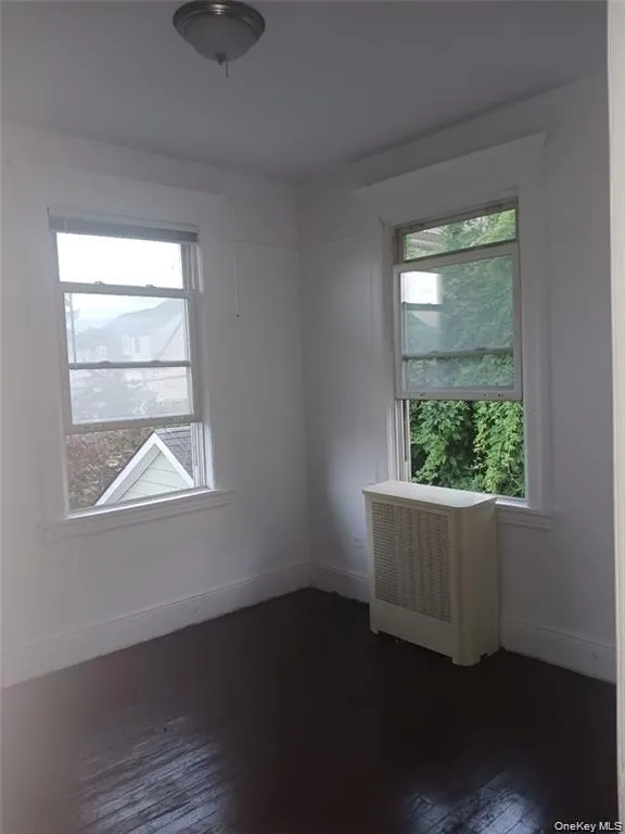 Spare room with radiator heating unit, dark wood finished floors, and healthy amount of natural light Spare room with radiator heating unit, dark wood finished floors, and healthy amount of natural light