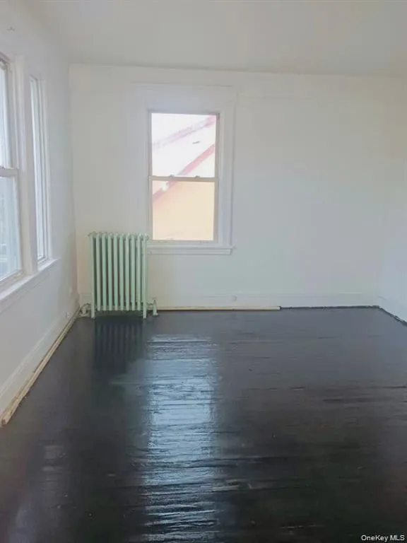 Unfurnished room with radiator heating unit and dark wood-style flooring Unfurnished room with radiator heating unit and dark wood-style flooring