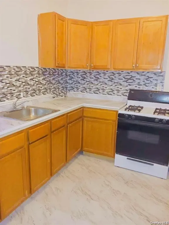 Kitchen featuring gas stove, light countertops, tasteful backsplash, brown cabinets, and light marble finish floors Kitchen featuring gas stove, light countertops, tasteful backsplash, brown cabinets, and light marble finish floors