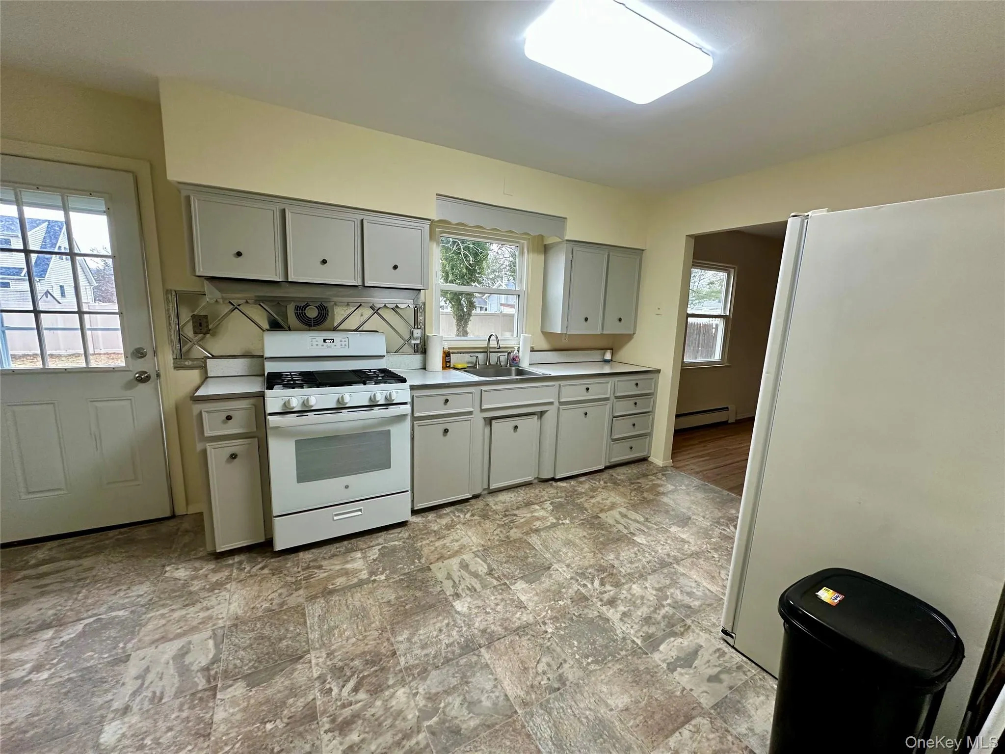 Kitchen featuring white appliances, light countertops, gray cabinets, and a baseboard heating unit Kitchen featuring white appliances, light countertops, gray cabinets, and a baseboard heating unit