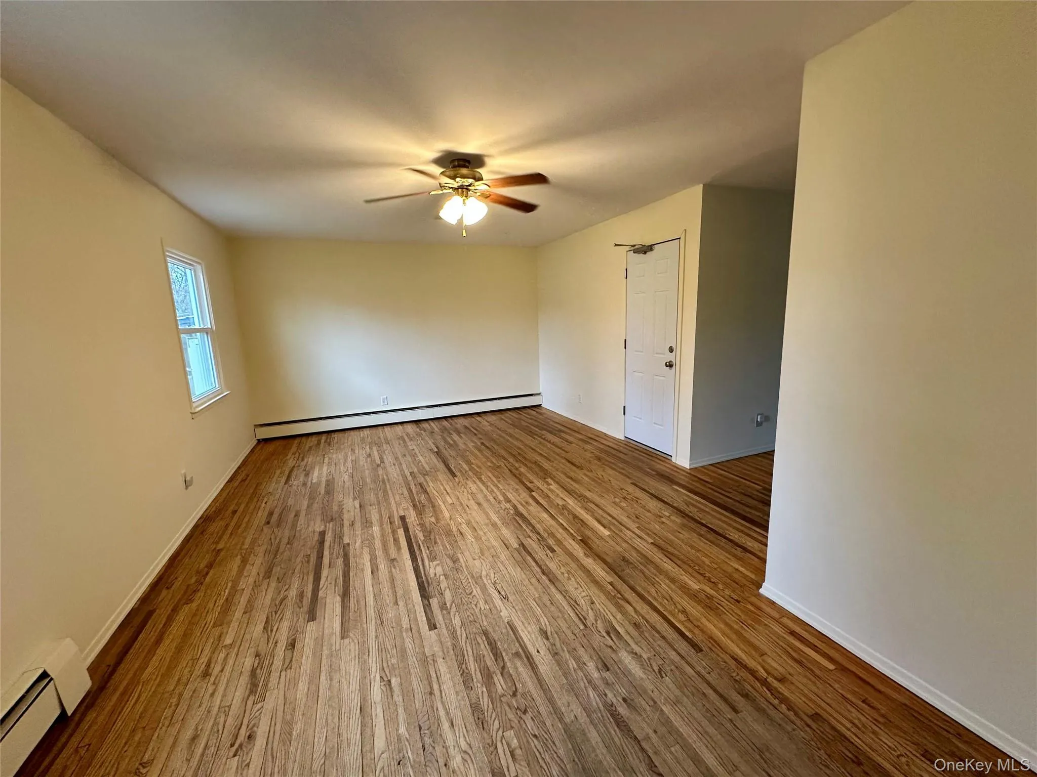 Empty room featuring a baseboard radiator, wood finished floors, and ceiling fan Empty room featuring a baseboard radiator, wood finished floors, and ceiling fan