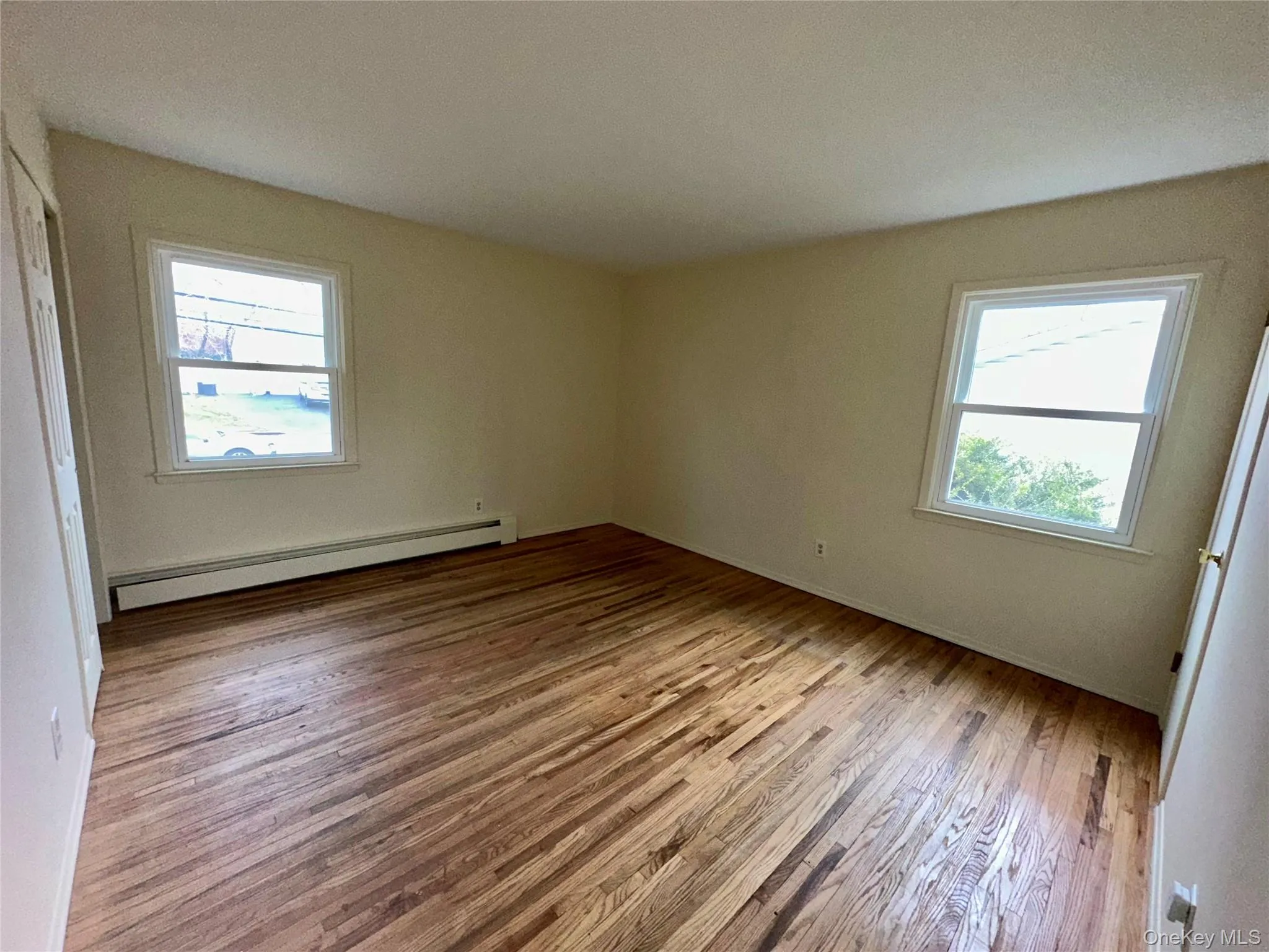 Unfurnished bedroom with a baseboard radiator, light wood finished floors, and a textured ceiling Unfurnished bedroom with a baseboard radiator, light wood finished floors, and a textured ceiling