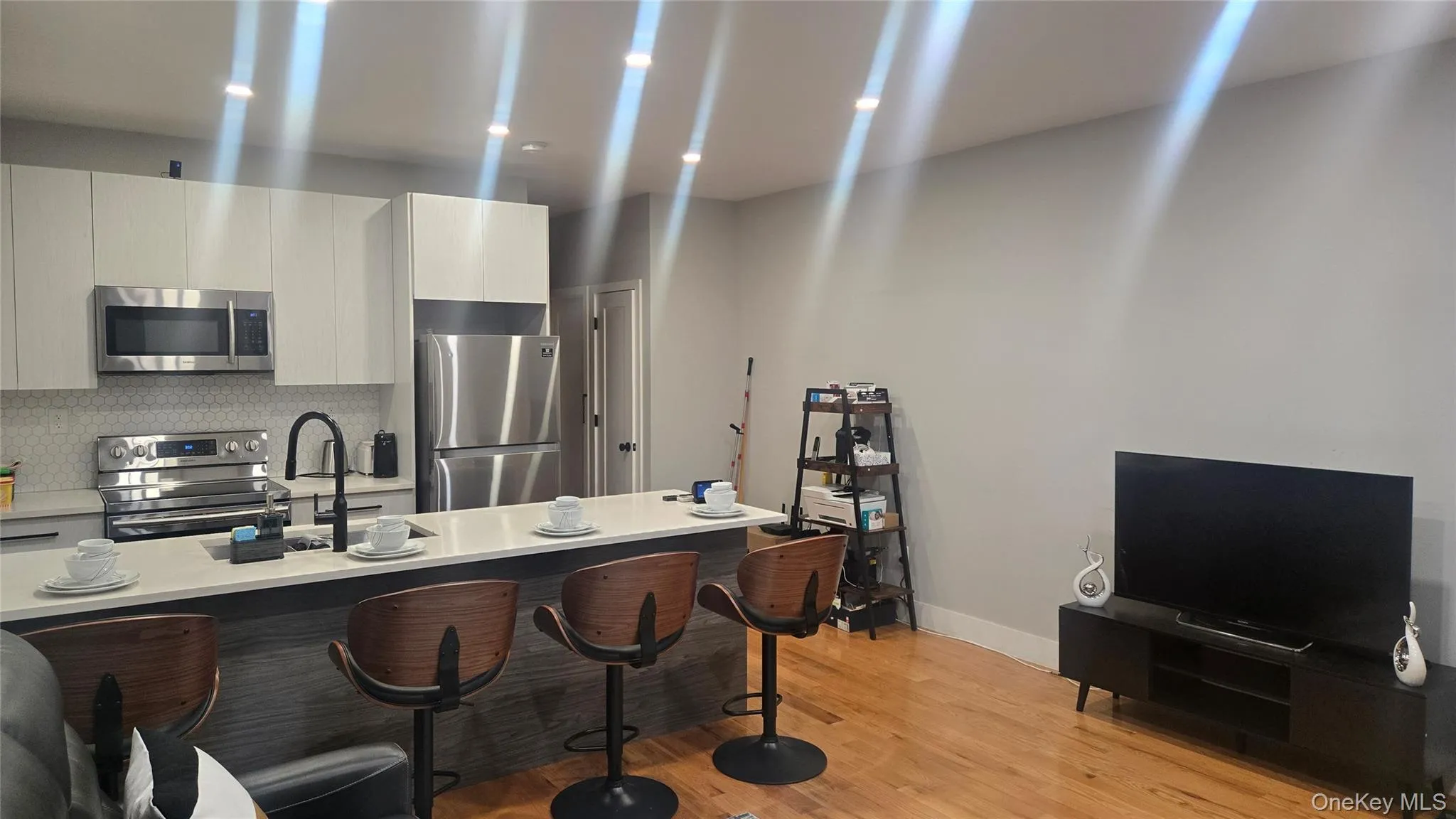 Kitchen featuring modern cabinets, stainless steel appliances, a kitchen breakfast bar, decorative backsplash, and light wood-style floors Kitchen featuring modern cabinets, stainless steel appliances, a kitchen breakfast bar, decorative backsplash, and light wood-style floors