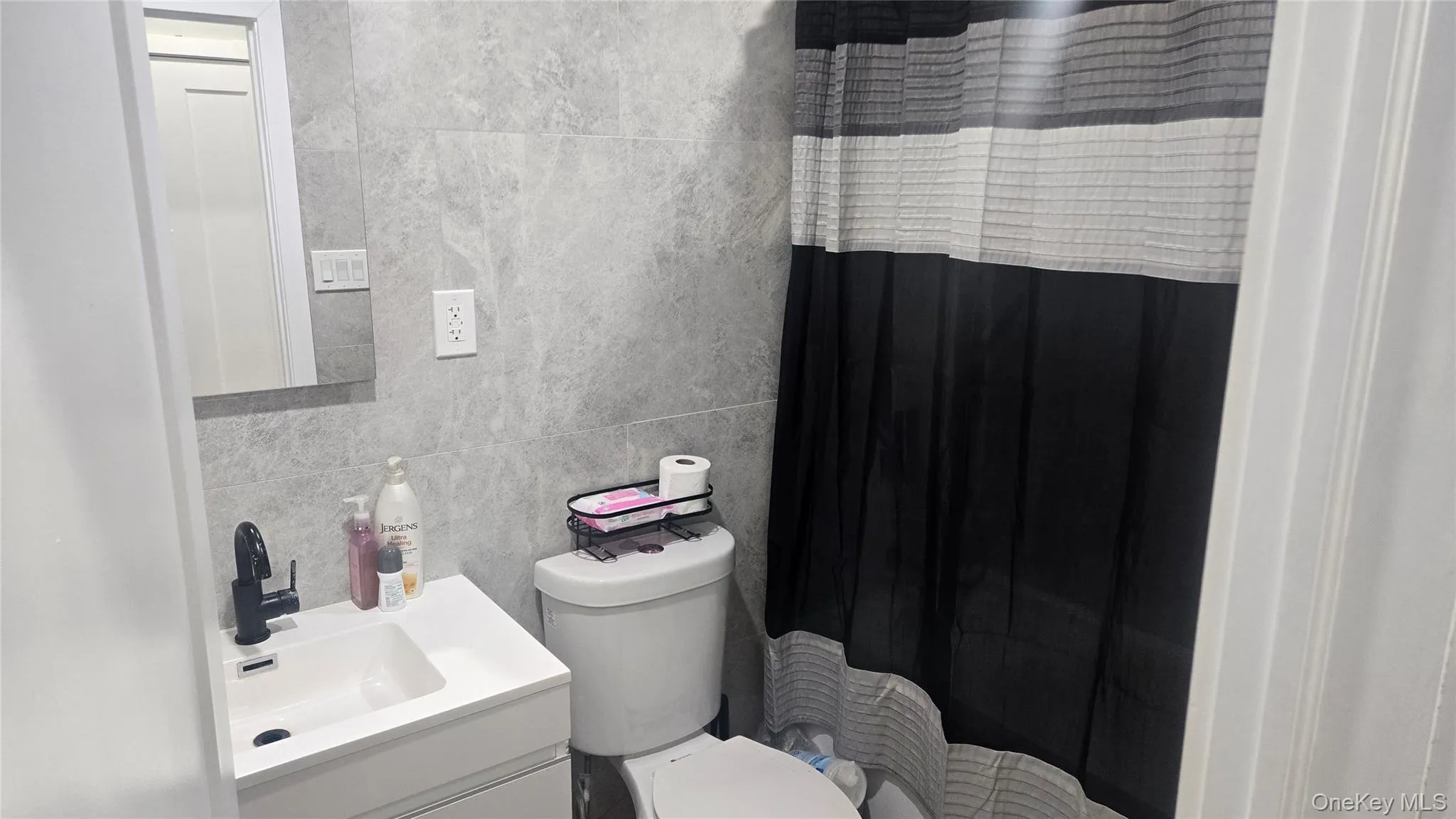 Full bath with tile walls, a shower with curtain, vanity, and backsplash Full bath with tile walls, a shower with curtain, vanity, and backsplash