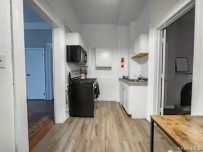 Kitchen with white cabinetry, range, light wood-style flooring, and black microwave Kitchen with white cabinetry, range, light wood-style flooring, and black microwave