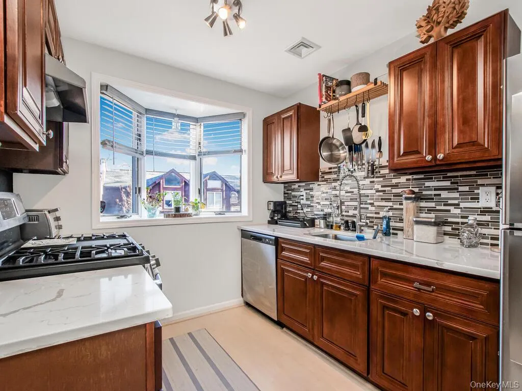 Kitchen featuring light stone countertops, appliances with stainless steel finishes, decorative backsplash, and ventilation hood Kitchen featuring light stone countertops, appliances with stainless steel finishes, decorative backsplash, and ventilation hood