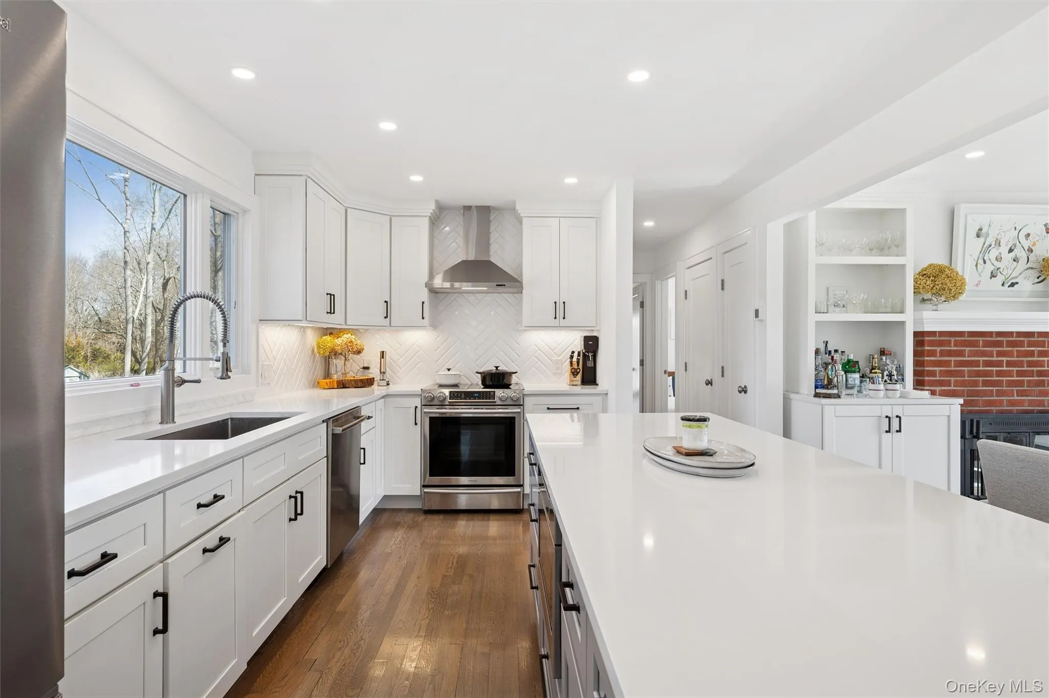 Kitchen featuring wall chimney exhaust hood, a sink, light countertops, stainless steel appliances, and decorative backsplash Kitchen featuring wall chimney exhaust hood, a sink, light countertops, stainless steel appliances, and decorative backsplash