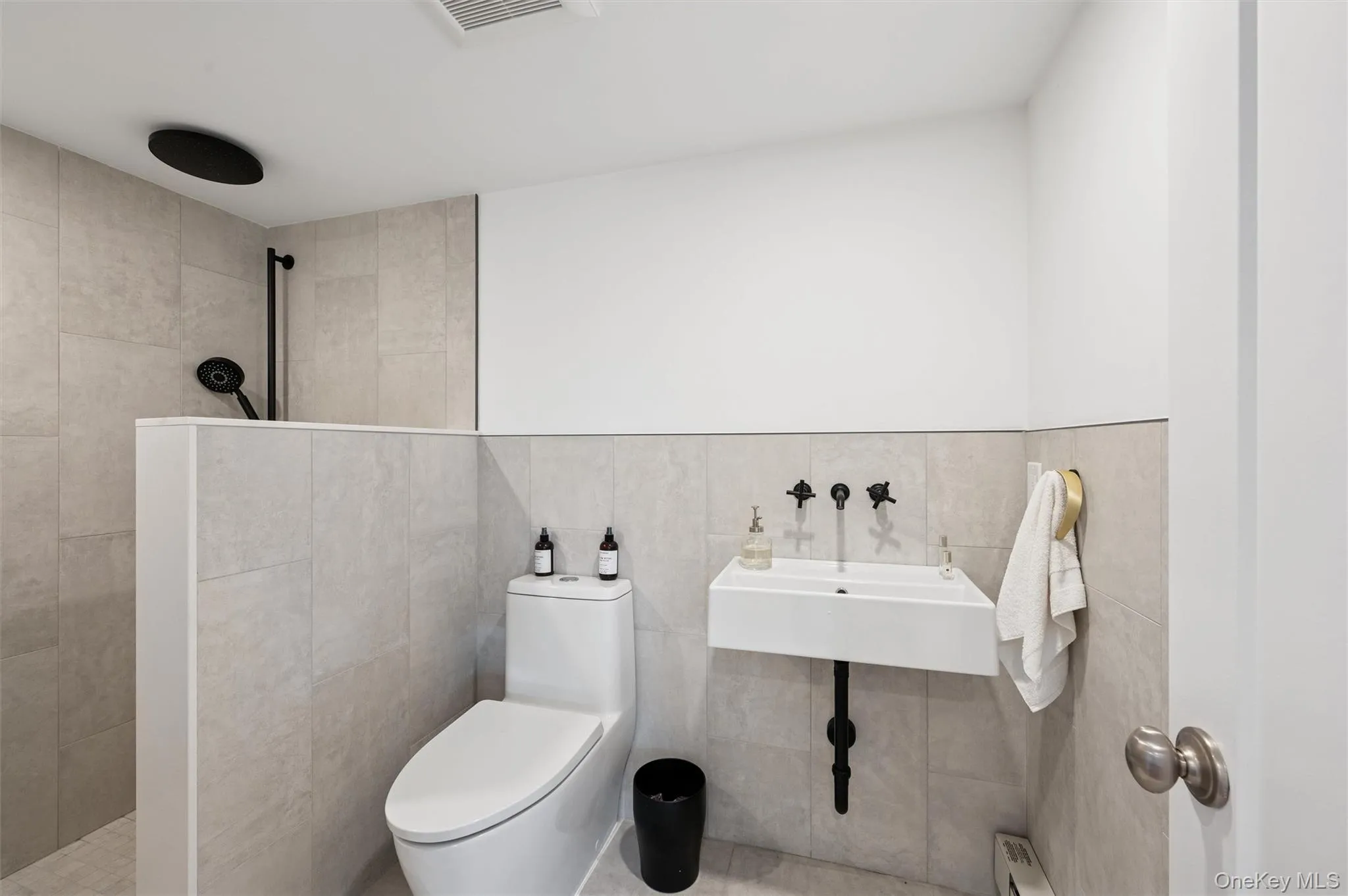 Bathroom with a walk in shower, visible vents, toilet, tile walls, and a baseboard radiator Bathroom with a walk in shower, visible vents, toilet, tile walls, and a baseboard radiator