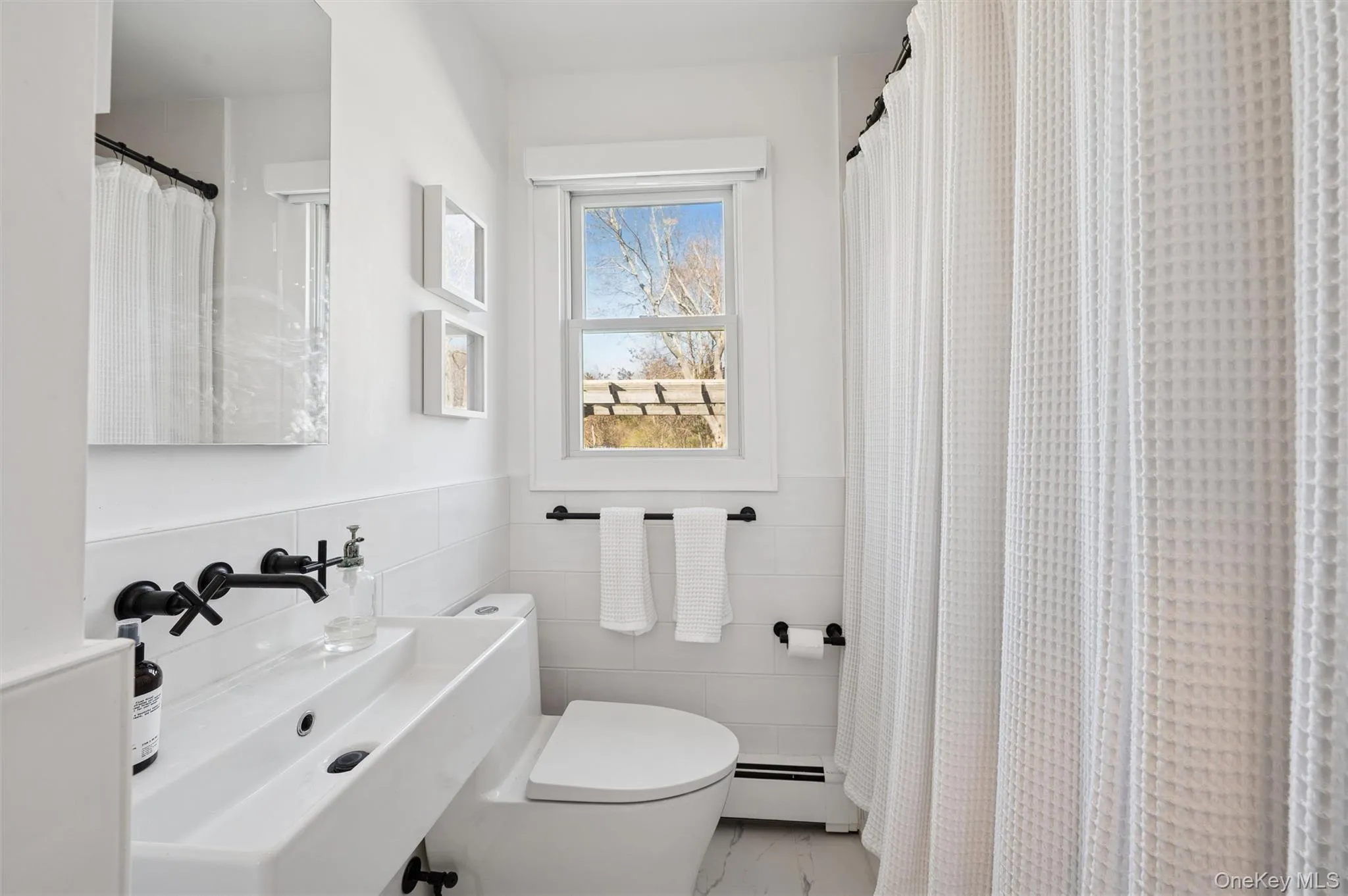 Full bath featuring a baseboard heating unit, a wainscoted wall, toilet, marble finish floor, and a sink Full bath featuring a baseboard heating unit, a wainscoted wall, toilet, marble finish floor, and a sink