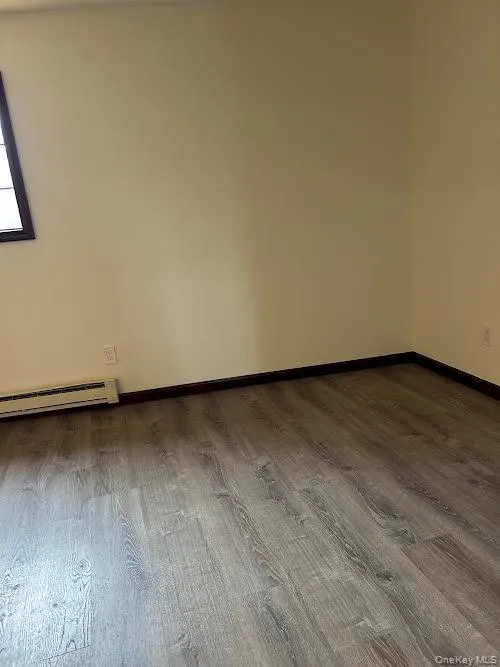 Unfurnished room with a baseboard radiator and dark wood-style floors Unfurnished room with a baseboard radiator and dark wood-style floors