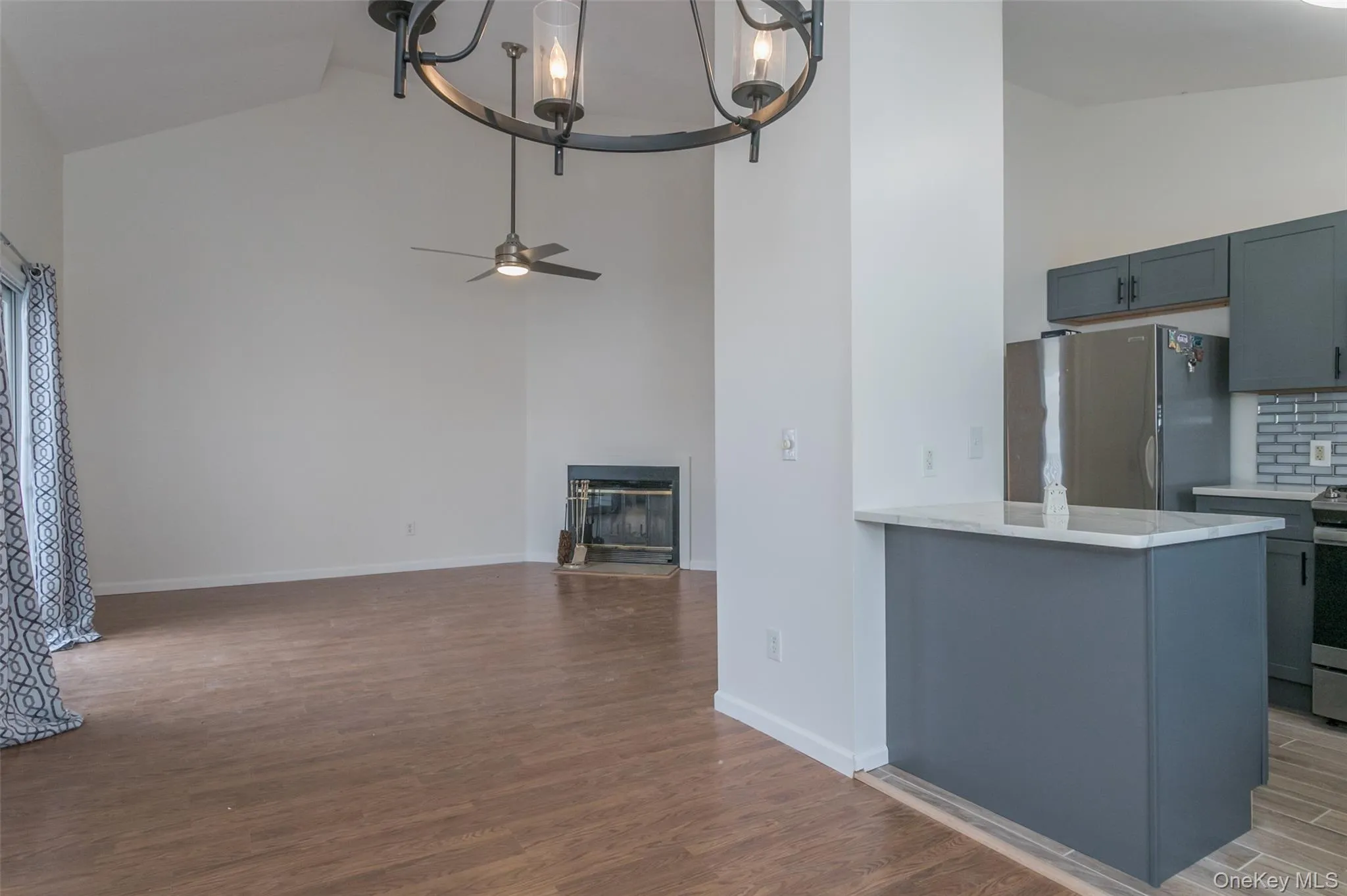 Kitchen featuring gray cabinets, light wood-type flooring, appliances with stainless steel finishes, high vaulted ceiling, and backsplash Kitchen featuring gray cabinets, light wood-type flooring, appliances with stainless steel finishes, high vaulted ceiling, and backsplash