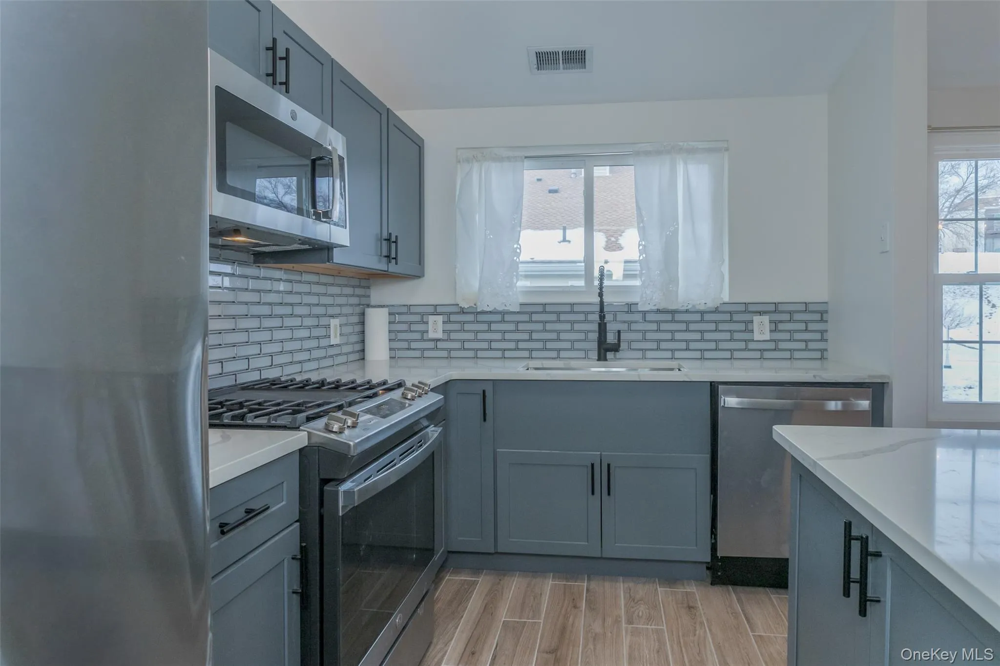Kitchen featuring stainless steel appliances, gray cabinetry, and light stone counters Kitchen featuring stainless steel appliances, gray cabinetry, and light stone counters