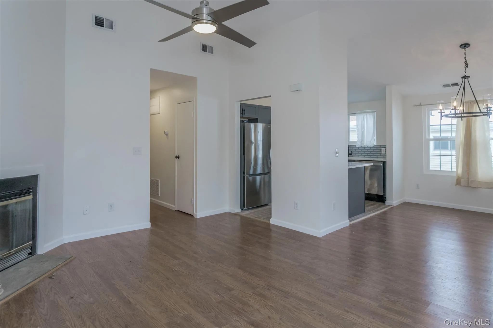 Unfurnished living room featuring dark wood-type flooring, a glass covered fireplace, ceiling fan, and a chandelier Unfurnished living room featuring dark wood-type flooring, a glass covered fireplace, ceiling fan, and a chandelier