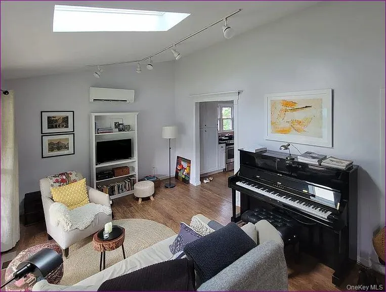 Living room featuring vaulted ceiling, a skylight, rail lighting, wood finished floors, and a wall unit AC Living room featuring vaulted ceiling, a skylight, rail lighting, wood finished floors, and a wall unit AC