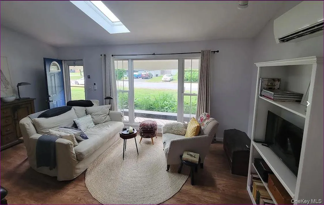 Living area featuring a wall mounted AC, a skylight, and dark wood-style flooring Living area featuring a wall mounted AC, a skylight, and dark wood-style flooring
