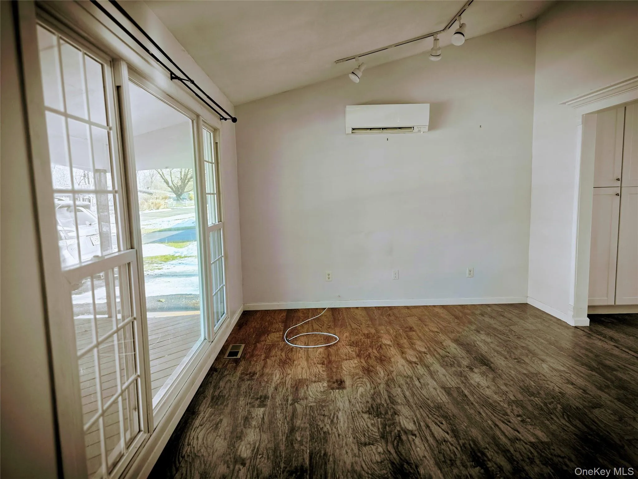 Spare room with lofted ceiling, dark wood-type flooring, a wall mounted AC, and track lighting Spare room with lofted ceiling, dark wood-type flooring, a wall mounted AC, and track lighting