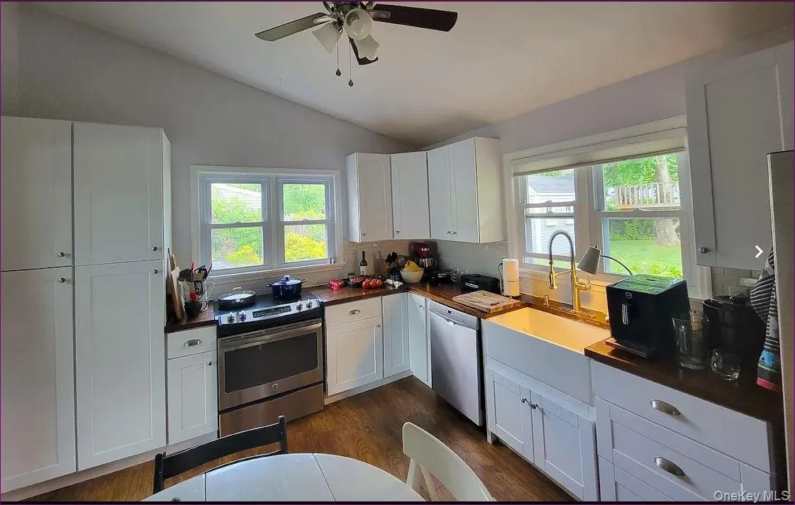 Kitchen featuring white cabinetry, stainless steel appliances, lofted ceiling, dark wood-style flooring, and ceiling fan Kitchen featuring white cabinetry, stainless steel appliances, lofted ceiling, dark wood-style flooring, and ceiling fan