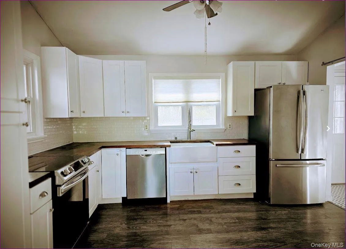 Kitchen with stainless steel appliances, white cabinetry, dark wood-type flooring, and tasteful backsplash Kitchen with stainless steel appliances, white cabinetry, dark wood-type flooring, and tasteful backsplash