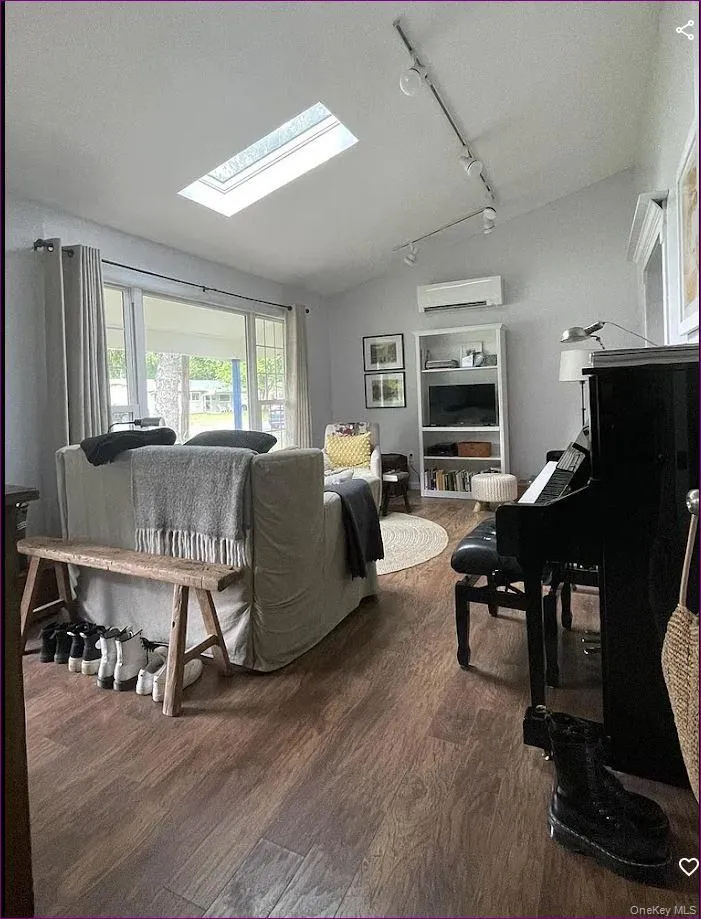 Living area featuring lofted ceiling, a skylight, rail lighting, dark wood-style flooring, and a wall unit AC Living area featuring lofted ceiling, a skylight, rail lighting, dark wood-style flooring, and a wall unit AC