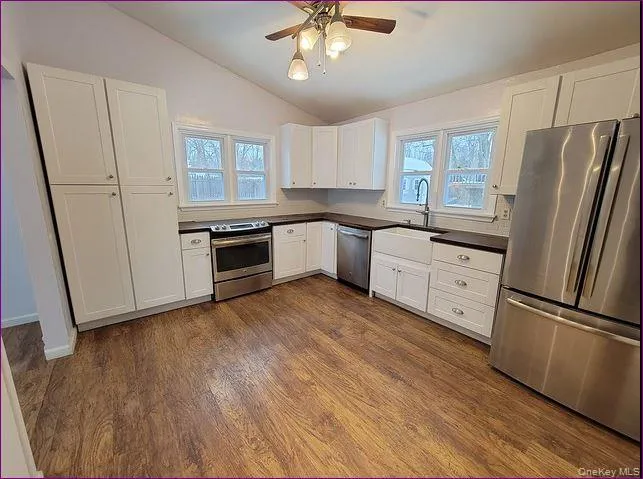 Kitchen with stainless steel appliances, dark countertops, lofted ceiling, white cabinets, and healthy amount of natural light Kitchen with stainless steel appliances, dark countertops, lofted ceiling, white cabinets, and healthy amount of natural light