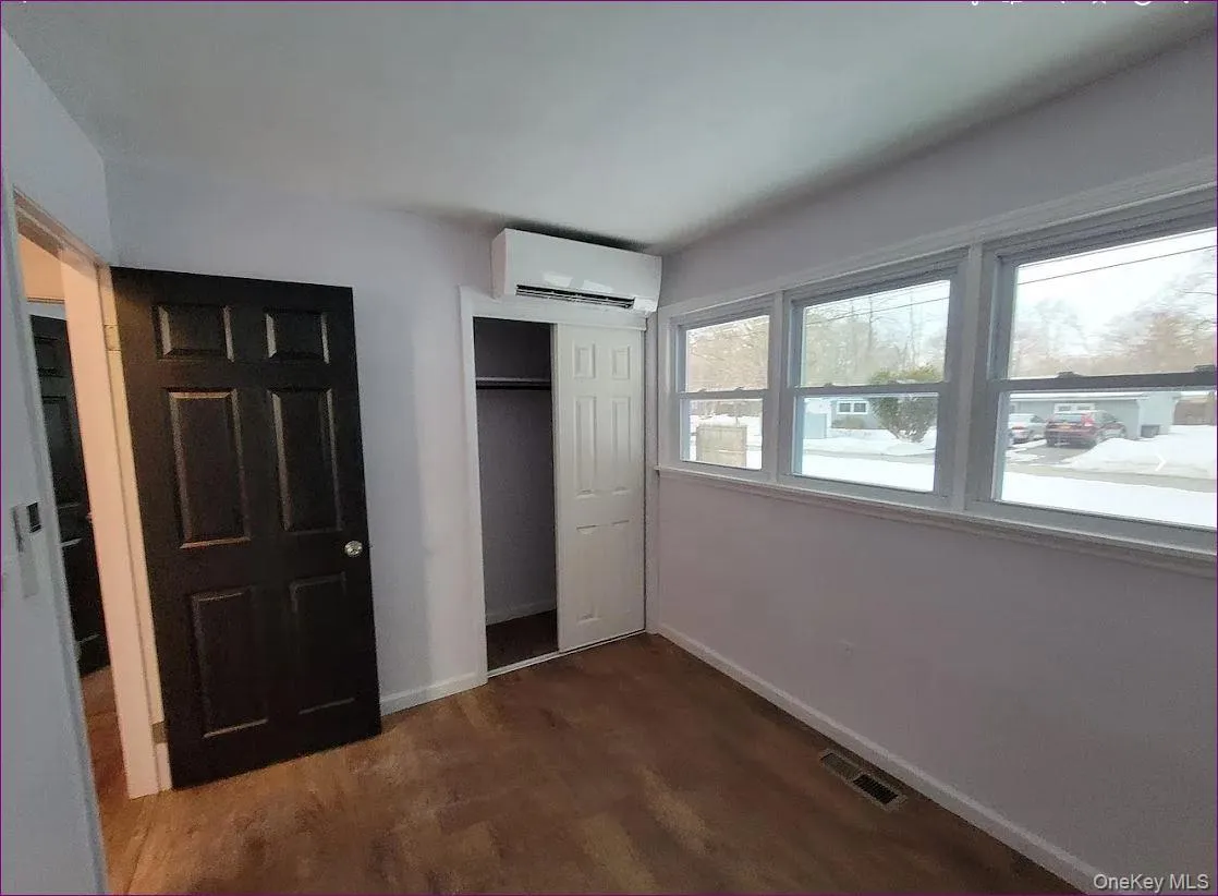 Unfurnished bedroom featuring a closet, dark wood-style floors, and an AC wall unit Unfurnished bedroom featuring a closet, dark wood-style floors, and an AC wall unit