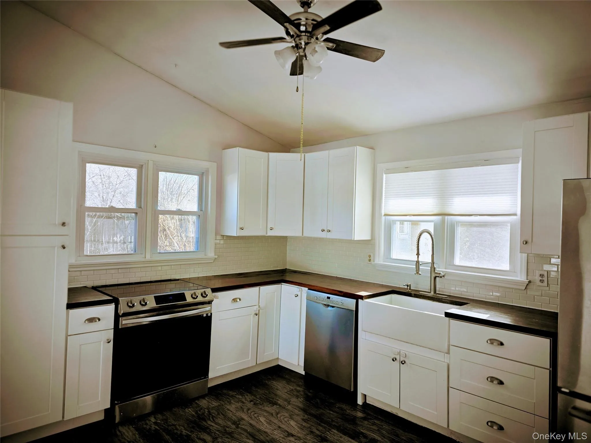 Kitchen featuring appliances with stainless steel finishes, lofted ceiling, white cabinets, decorative backsplash, and dark wood-style floors Kitchen featuring appliances with stainless steel finishes, lofted ceiling, white cabinets, decorative backsplash, and dark wood-style floors