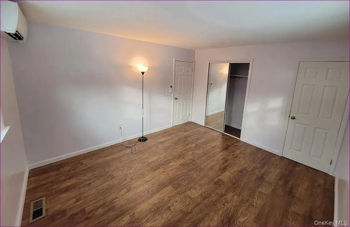 Unfurnished bedroom with a wall mounted AC, dark wood-type flooring, and a closet Unfurnished bedroom with a wall mounted AC, dark wood-type flooring, and a closet