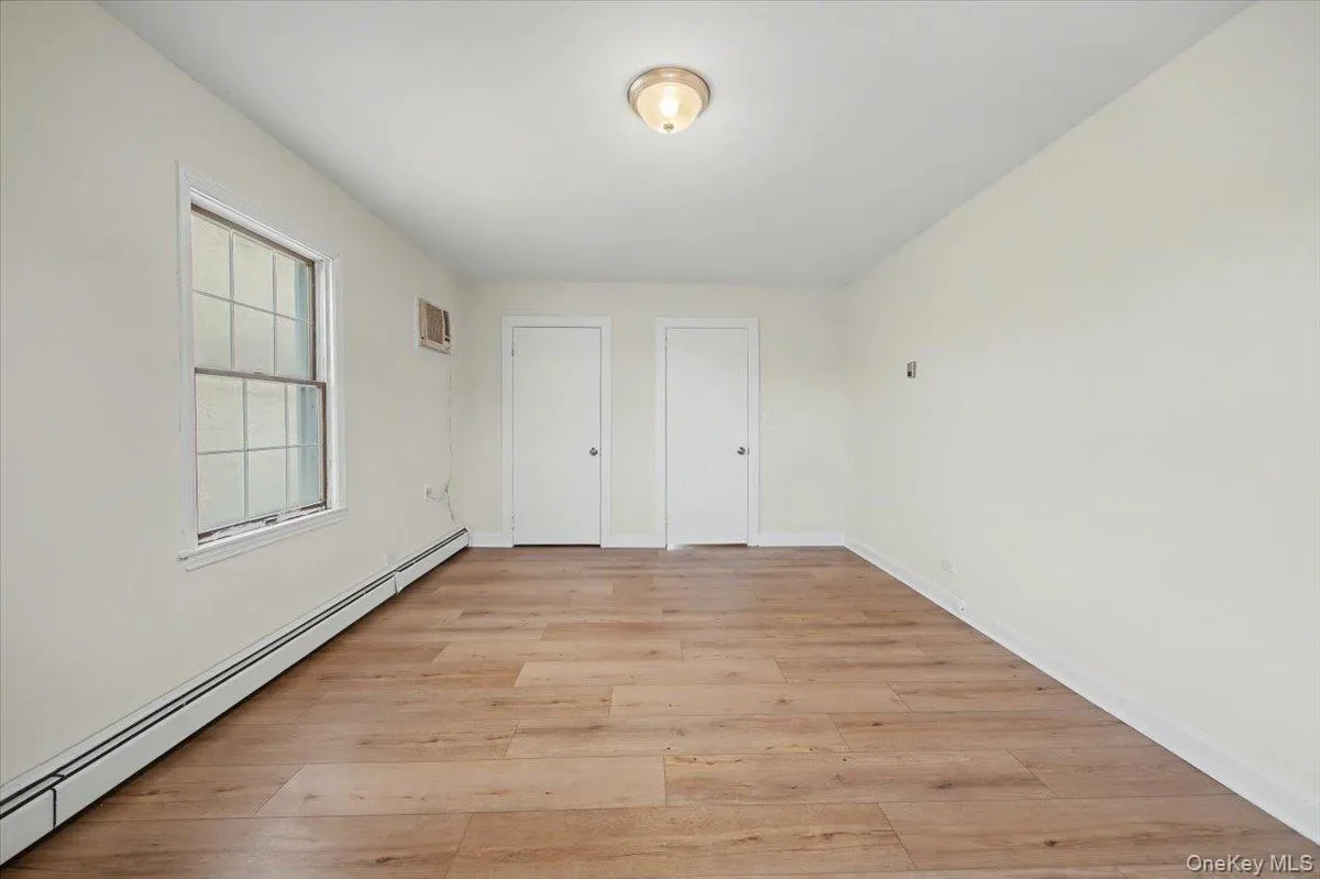 Unfurnished bedroom with baseboard heating, multiple closets, and light wood-style floors Unfurnished bedroom with baseboard heating, multiple closets, and light wood-style floors