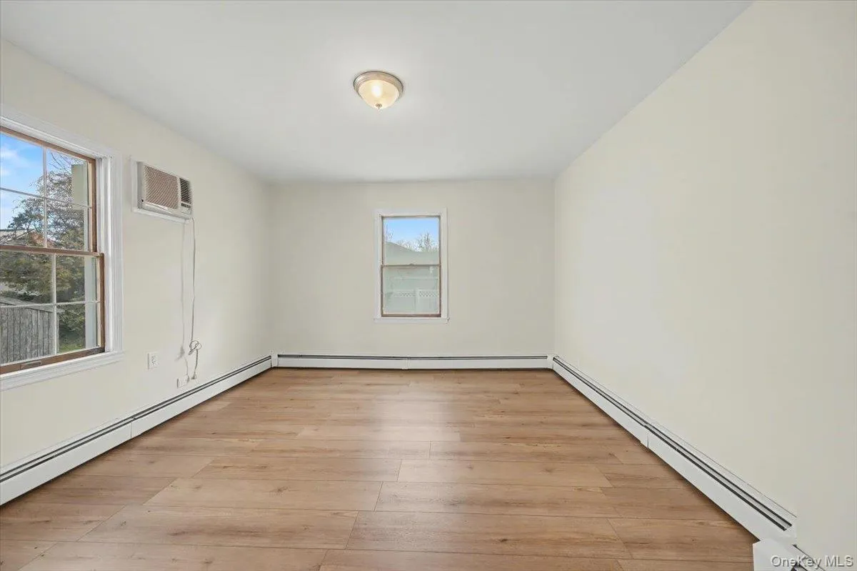 Spare room featuring a baseboard heating unit, light wood-style floors, and an AC wall unit Spare room featuring a baseboard heating unit, light wood-style floors, and an AC wall unit