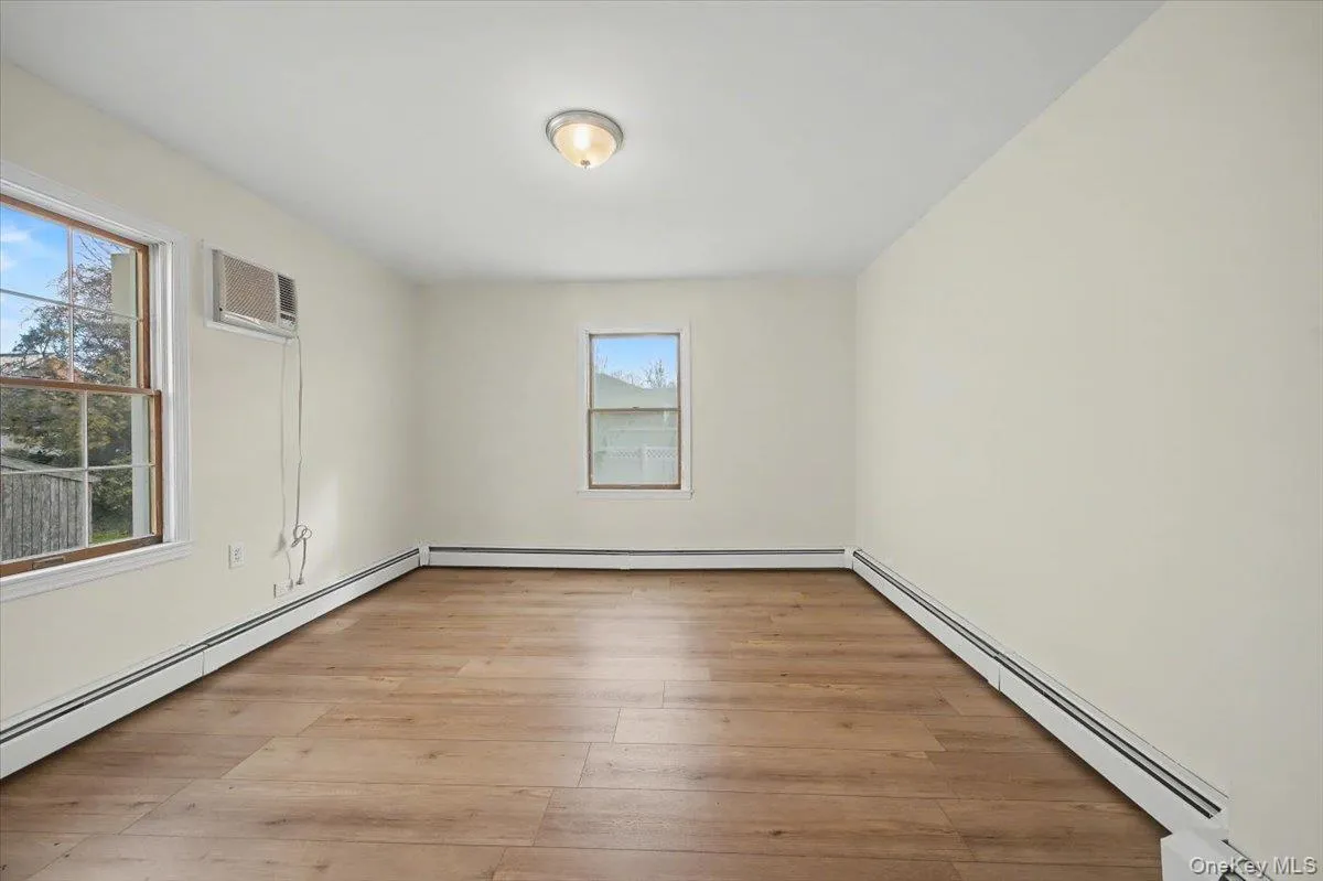 Unfurnished room featuring baseboard heating, light wood finished floors, and a wall mounted air conditioner Unfurnished room featuring baseboard heating, light wood finished floors, and a wall mounted air conditioner