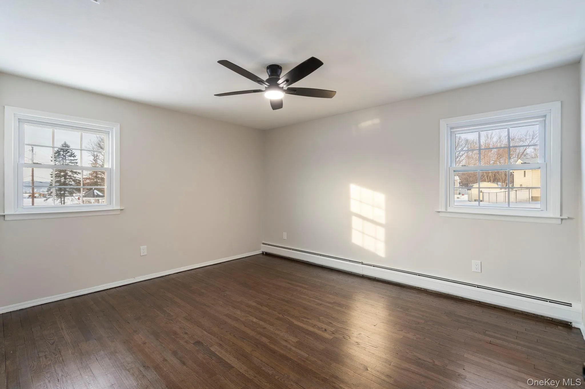 Spare room featuring baseboard heating, dark wood finished floors, and ceiling fan Spare room featuring baseboard heating, dark wood finished floors, and ceiling fan