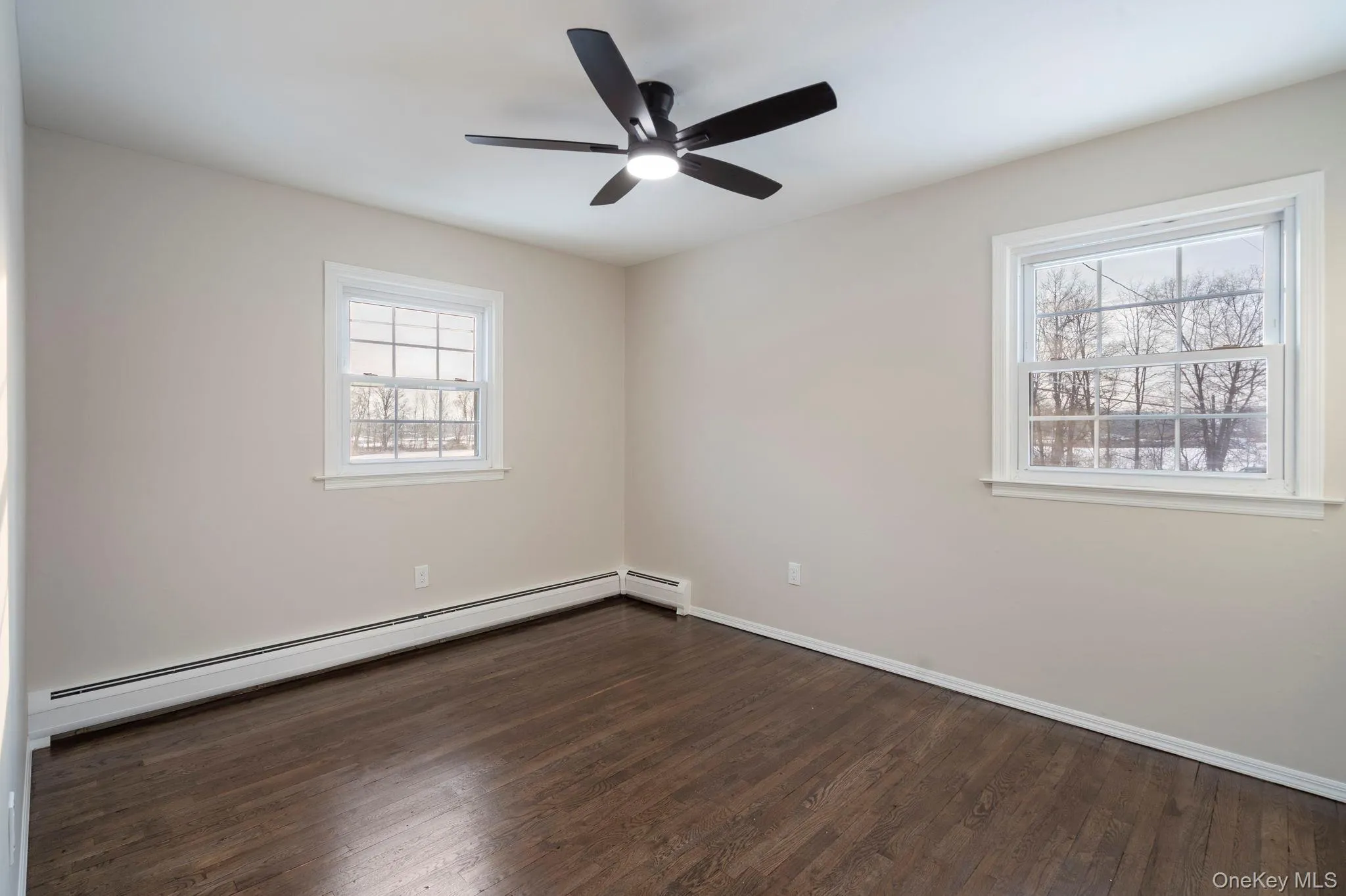 Empty room with dark wood finished floors, baseboard heating, and a ceiling fan Empty room with dark wood finished floors, baseboard heating, and a ceiling fan